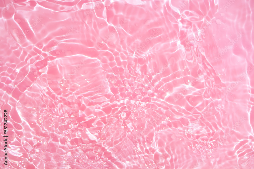 Fototapeta premium Defocus blurred transparent pink colored clear calm water surface texture with splashes and bubbles. Trendy abstract nature background. Water waves in sunlight with copy space. Pink watercolor shining