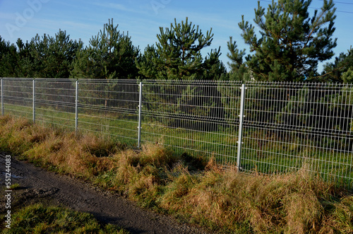 a solid wire fence encloses the garden. the welded wire meshes are strong and can be inserted between the prisms of the bars. the posts are concreted into the concrete slab fence, meadow