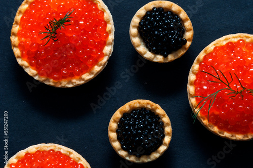 Red and black caviar in tartlets on a black background.