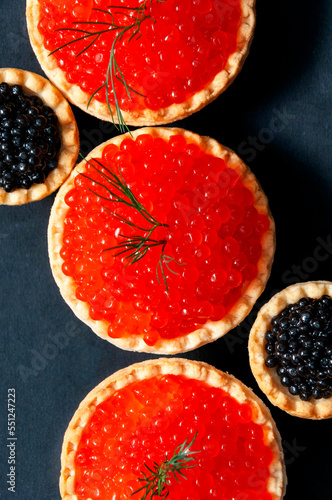Red and black caviar in tartlets on a black background.