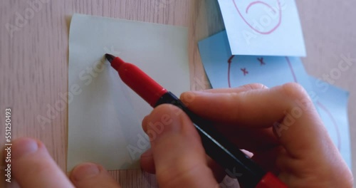 Man draws a funny smiling face with a red felt-tip pen on a sticker glued to the wall. The concept of motivation, optimism, victory, psychology, emotions. 4K 4096x2160