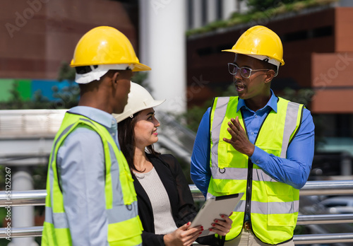 black executive engineer working at construction site outside building in city and talking with caucasian businesswoman and black engineer