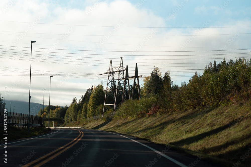 High powered energy cables next to empty road during sunrise.