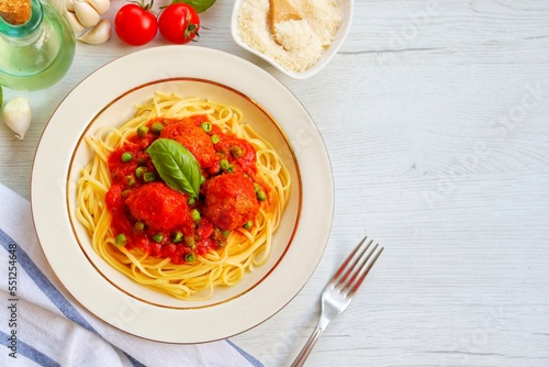 Italian Traditional Dish"Spaghetti con polpette e piselli",spaghetti with meatballs and green peas in tomato sauce on plate with white wood background.Top view.Copy space