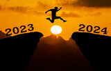 A young man jump between 2023 and 2024 years over the sun and through on the gap of hill  silhouette evening colorful sky. happy new year 2023.