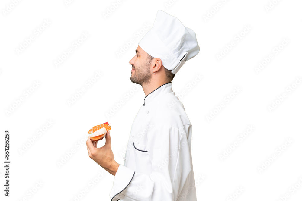 Young caucasian chef holding a sushi over isolated background laughing in lateral position Young caucasian chef holding a sushi over isolated background laughing in lateral position