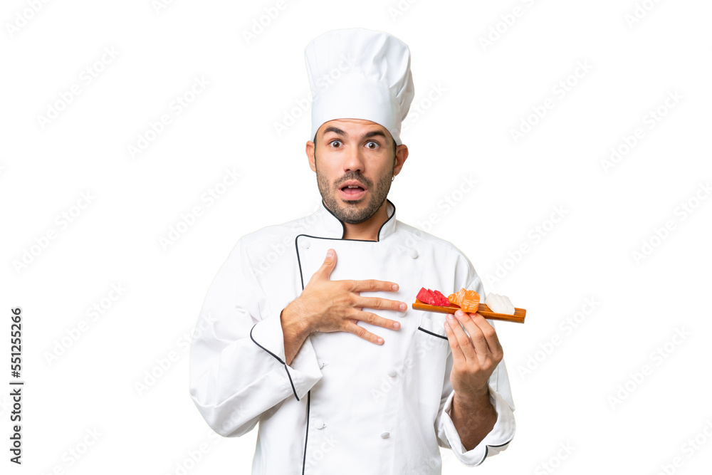 Young caucasian chef holding a sushi over isolated background surprised and shocked while looking right Young caucasian chef holding a sushi over isolated background surprised and shocked while looking right