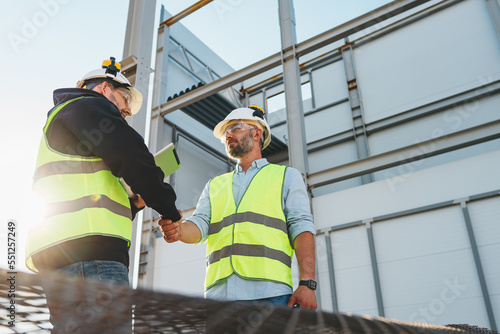 Handshake of two engineers wearing safety helmet and protect sunglasses on outdoors construction site. Meeting and hand shake of engineers and worker photo
