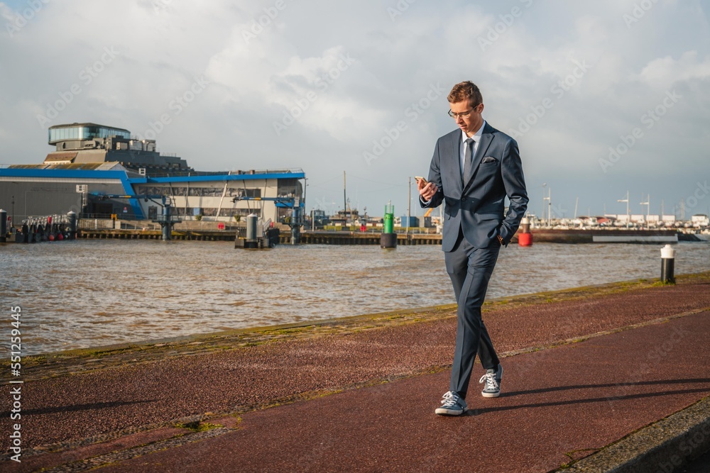 Young businessman walking casually while looking at his phone. Businessman closely following his business Young businessman walking casually while looking at his phone. Businessman closely following his business