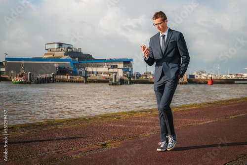 Young businessman walking casually while looking at his phone. Businessman closely following his business