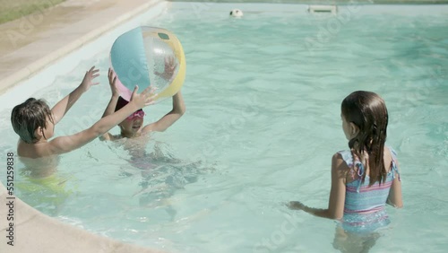 Children playing with inflatable ball in swimming pool outside. Group of boys and girls having fun, throwing ball to each other while standing in water. Childhood, summer, joy concept.