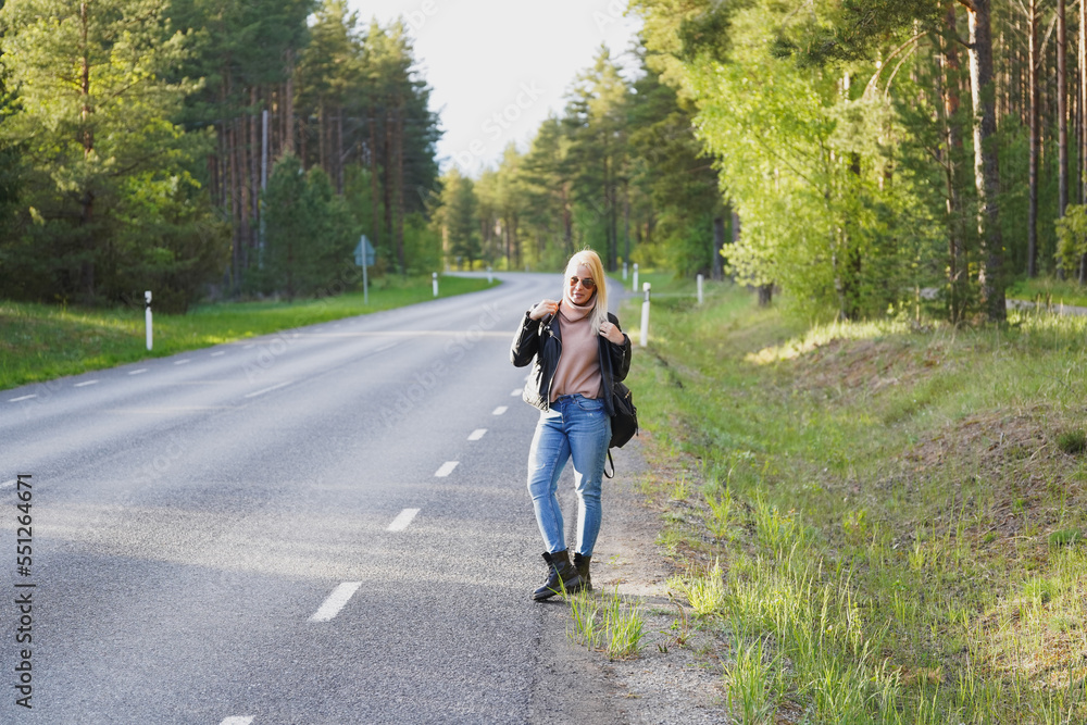 A beautiful blonde girl stands by the road in the forest on a spring day. A beautiful blonde girl stands by the road in the forest on a spring day.