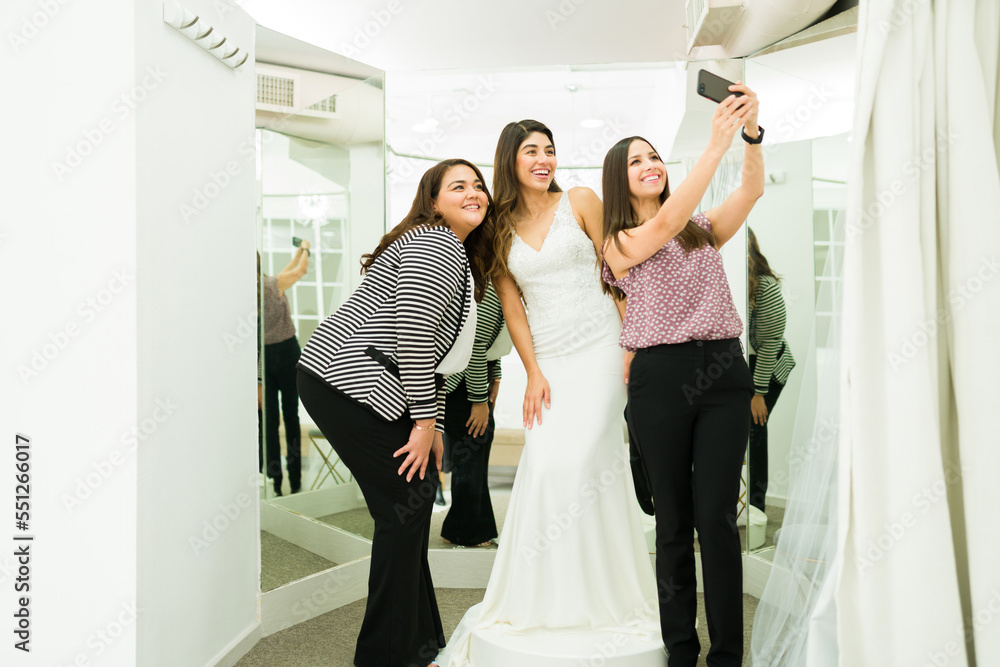 Young woman wearing a wedding dress in the dressing room with friends Young woman wearing a wedding dress in the dressing room with friends