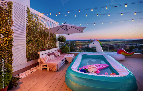 cozy rooftop patio with wooden pallet furniture, vertical garden and inflatable pool at warm summer evening photo