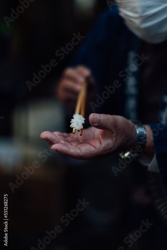 a hand holding chopsticks with rice on and another hand under the chopsticks.