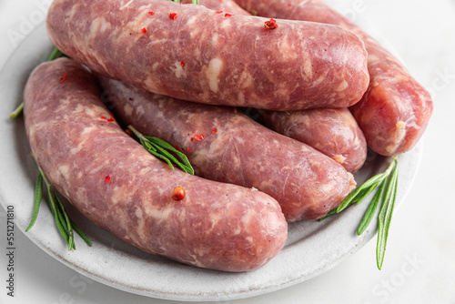 Raw sausages or bratwurst with spices and rosemary in a plate on white background. Close up