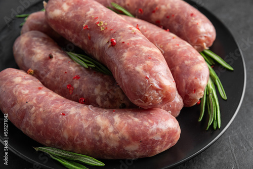 Raw sausages or bratwurst with spices and rosemary in a plate on black background. Close up