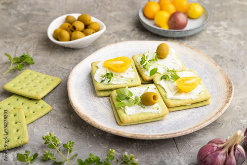 Green cracker sandwiches with cream cheese and tomatoes on gray concrete background. side view, close up.