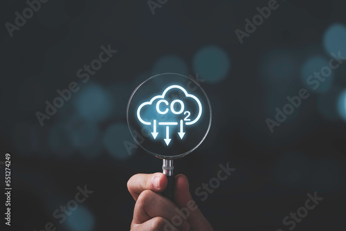 Hand holding CO2 reducing icon inside magnifier glass for focusing decrease CO2 or carbon dioxide emission ,carbon footprint and carbon credit to limit global warming from climate change concept.