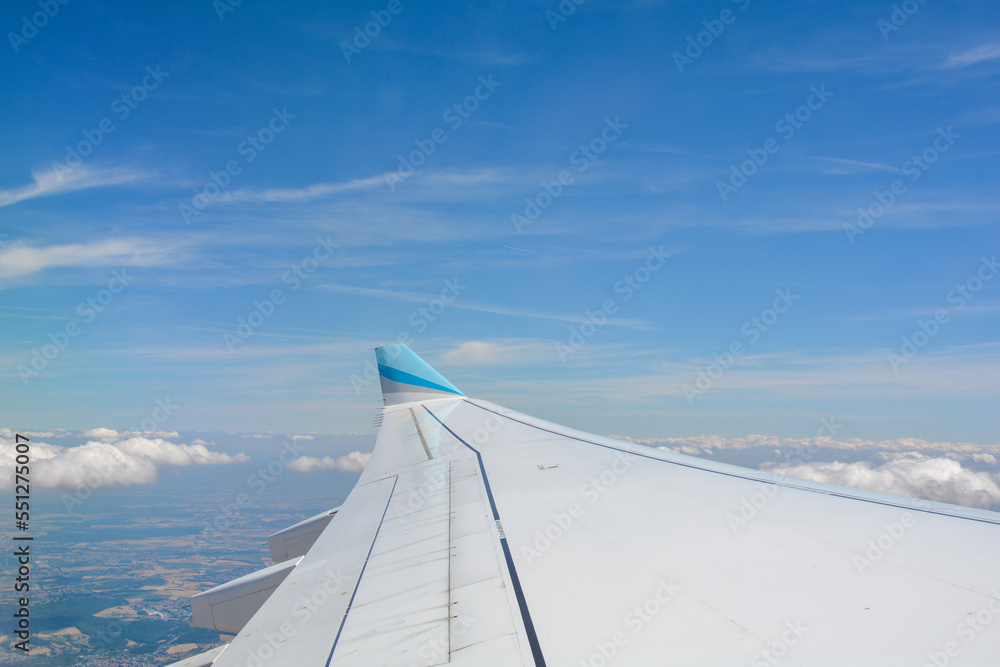 View from an airplane window showing the wing, sky, clouds and land