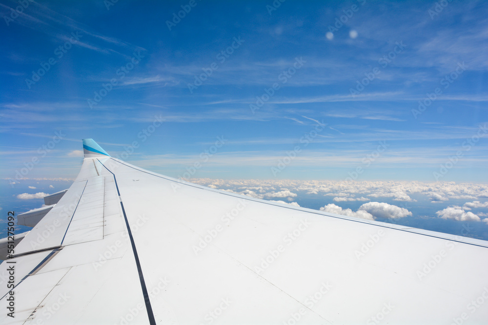 View from an airplane window showing the wing and sky with clouds View from an airplane window showing the wing and sky with clouds
