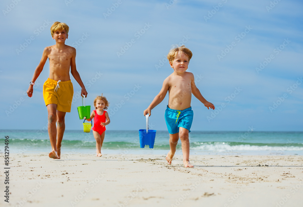 Three kids boys, girl run from ocean with bucket play on a beach