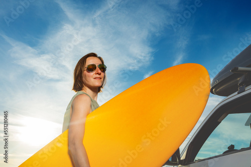 Close-up portrait of a young woman in sunglasses with surf board