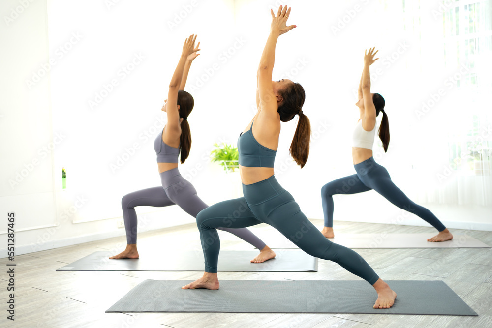 Young women are practicing yoga pose indoors for healthy lifestyle. Beautiful Asian female stretching, body balance and flexible muscle in fitness gym. Yoga exercising is mental and physical workout
