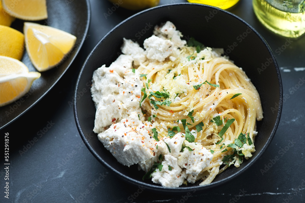 Spaghetti with ricotta cheese, lemon zest and chopped greens served in a black bowl, middle closeup, horizontal shot Spaghetti with ricotta cheese, lemon zest and chopped greens served in a black bowl, middle closeup, horizontal shot
