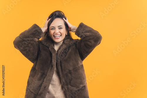 attractive and joyful young lady wearing a warm fur coat, glamour fashion model in stylish outfit posing to camera, medium shot orange background. High quality photo © PoppyPix