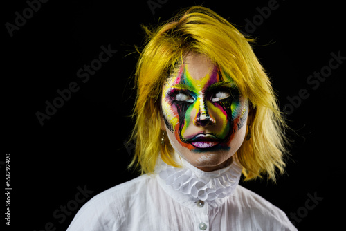 Portrait of woman with yellow hair and evil clown face art on black background