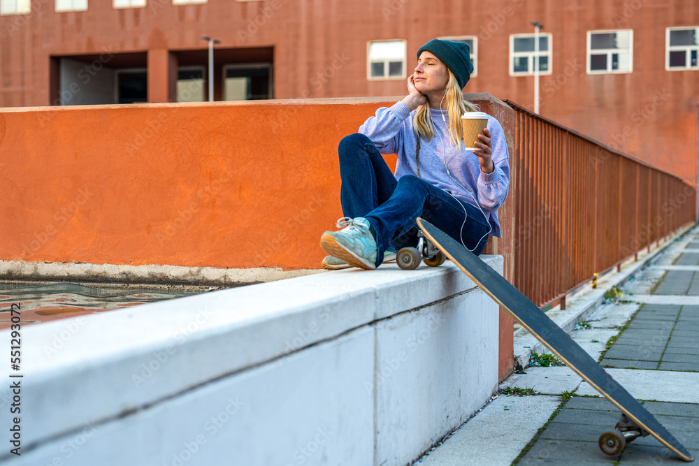 Young female teenager listens to music from her smartphone using headphones, relaxing moment of a skate girl, concept of street style and urban scene, Generation z people