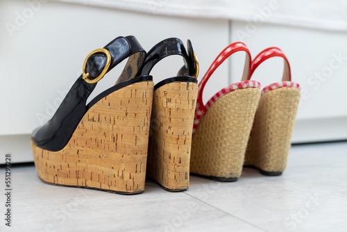 Photography Red and Black pair of open shoes with a high wedge heel in front of a closet