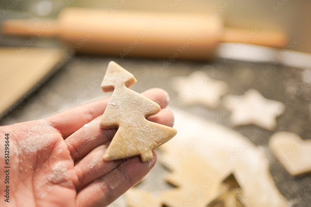 hand holding a christmas-tree shaped christmas cookie cut out of gingerbread dough. hand holding a christmas-tree shaped christmas cookie cut out of gingerbread dough.