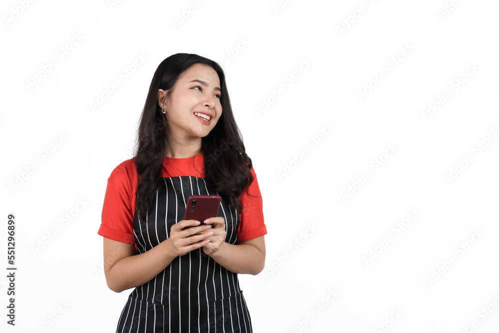 Holding mobile smartphone, Food shop owner concept, Smiling young confident asian woman in black apron and red t-shirt isolated on white background. Holding mobile smartphone, Food shop owner concept, Smiling young confident asian woman in black apron and red t-shirt isolated on white background.