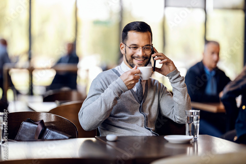 Photos A happy young man is talking on the phone in coffee shop while sipping coffee