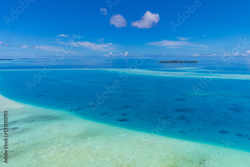 Aerial panorama of the blue lagoon bay in Maldives islands. Blue sea surface from above shallow ocean view. Horizon with sunny blue sky. Idyllic travel aerial seascape skyline. Tranquil blue wallpaper