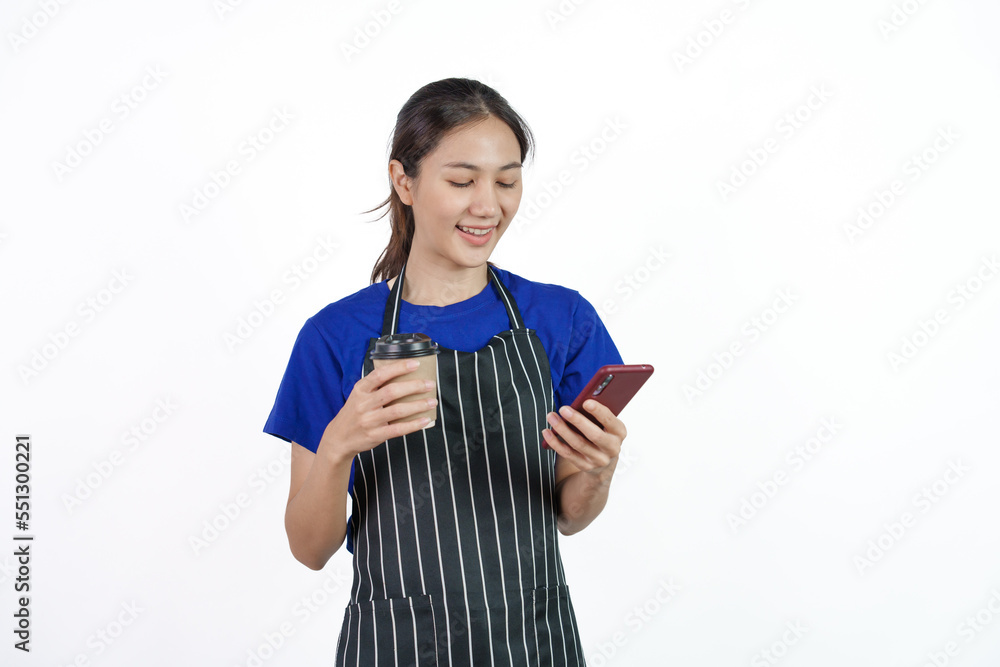 Excited asian coffee shop SME owner asian woman wearing blue t-shirt and black apron isolated on white background. Using phone and holding coffee cup Excited asian coffee shop SME owner asian woman wearing blue t-shirt and black apron isolated on white background. Using phone and holding coffee cup