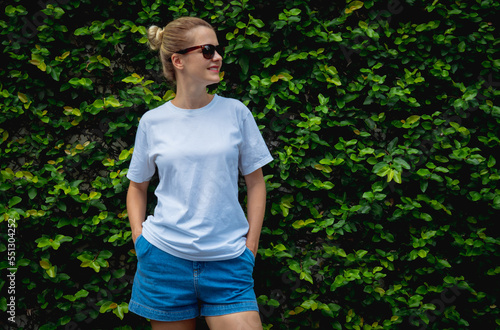 Female model wearing white blank t-shirt on the background of an leafes wall.