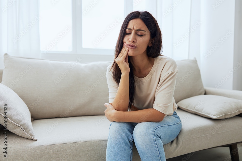 Woman toothache, tooth root inflammation sitting on sofa at home Woman toothache, tooth root inflammation sitting on sofa at home