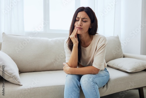 Woman toothache, tooth root inflammation sitting on sofa at home