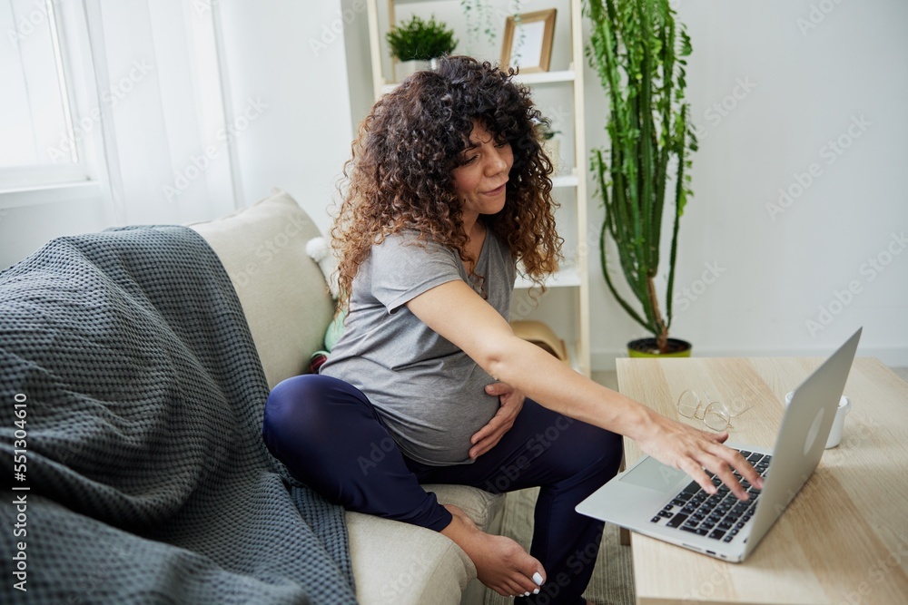 A pregnant woman sits on the sofa at home and orders goods for pregnant women on the Internet, online shopping. Home clothes, lifestyle of a pregnant woman, preparation for childbirth A pregnant woman sits on the sofa at home and orders goods for pregnant women on the Internet, online shopping. Home clothes, lifestyle of a pregnant woman, preparation for childbirth