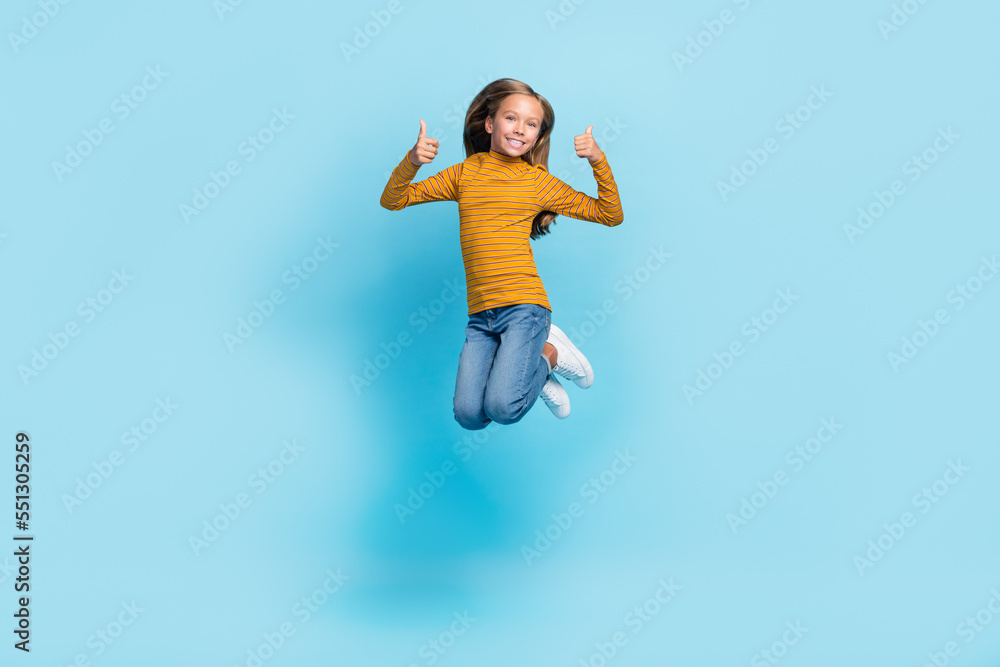 Obraz premium Full body portrait of cheerful girl jumping demonstrate thumbs up feedback isolated on blue color background
