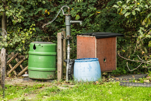 garden artwork in allotment of rain barrels, buckets and a pump