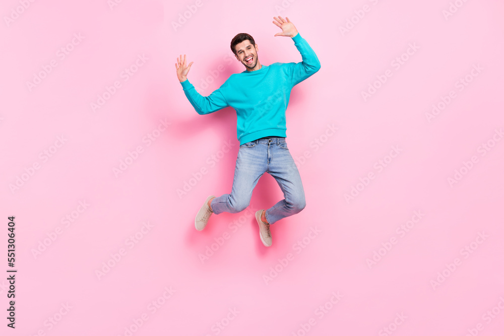 Full size photo of handsome young guy jumping raise hands excited have fun wear trendy blue garment isolated on pink color background Full size photo of handsome young guy jumping raise hands excited have fun wear trendy blue garment isolated on pink color background