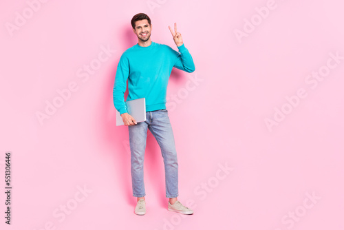 Full body photo of handsome young guy holding laptop entrepreneur showing v-sign wear trendy blue clothes isolated on pink color background