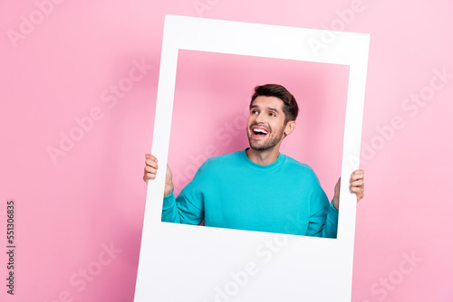 Photo portrait of handsome young man hold instant photo camera frame dressed stylish blue clothes isolated on pink color background