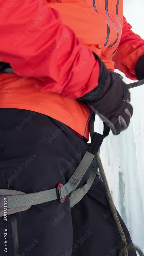 Vertical video of close up shot of Caucasian male ice climber tying a rope to his harness, preparing for a climb Vertical video of close up shot of Caucasian male ice climber tying a rope to his harness, preparing for a climb
