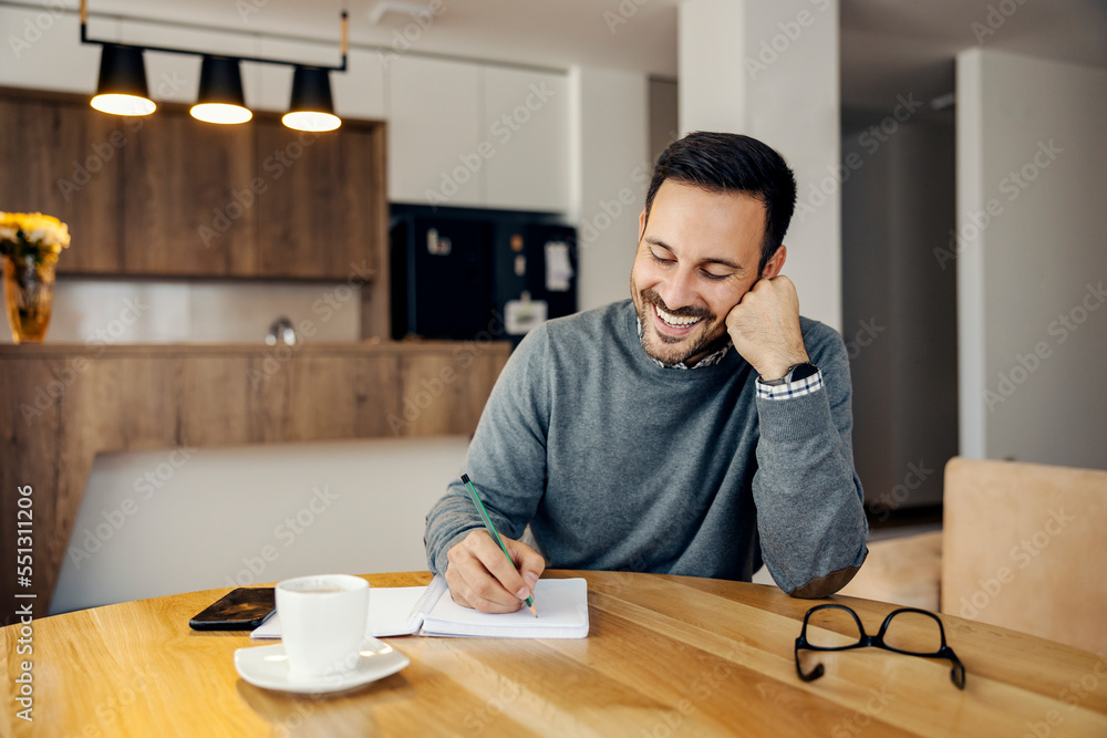 A smiling busy man is writing tasks in textbook at home. A smiling busy man is writing tasks in textbook at home.