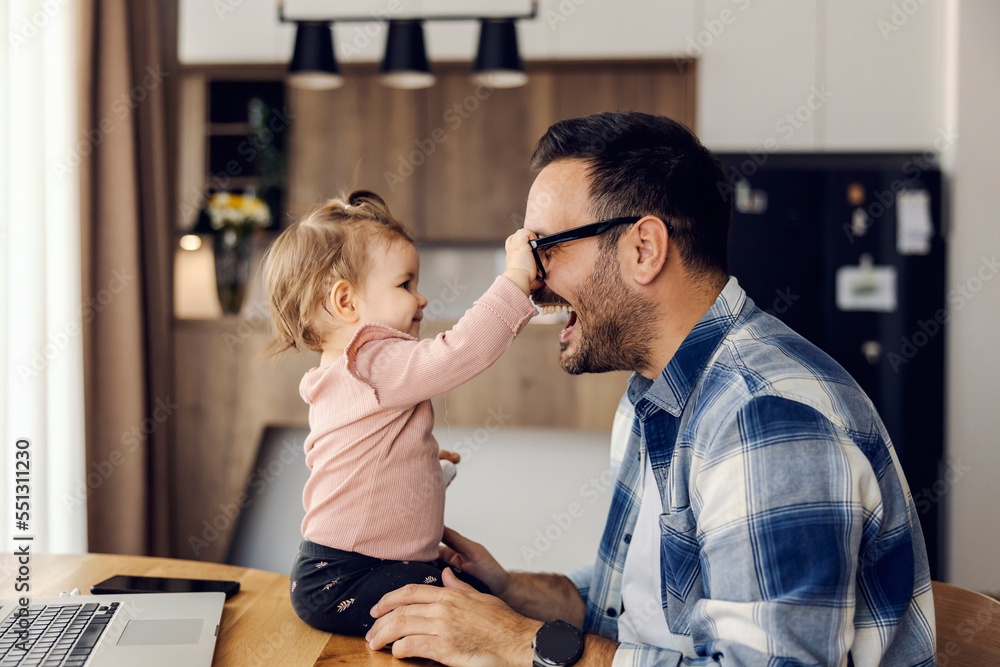 Fototapeta premium A silly baby girl is playing game with her dad. She is trying to take his eyeglasses on his work break.